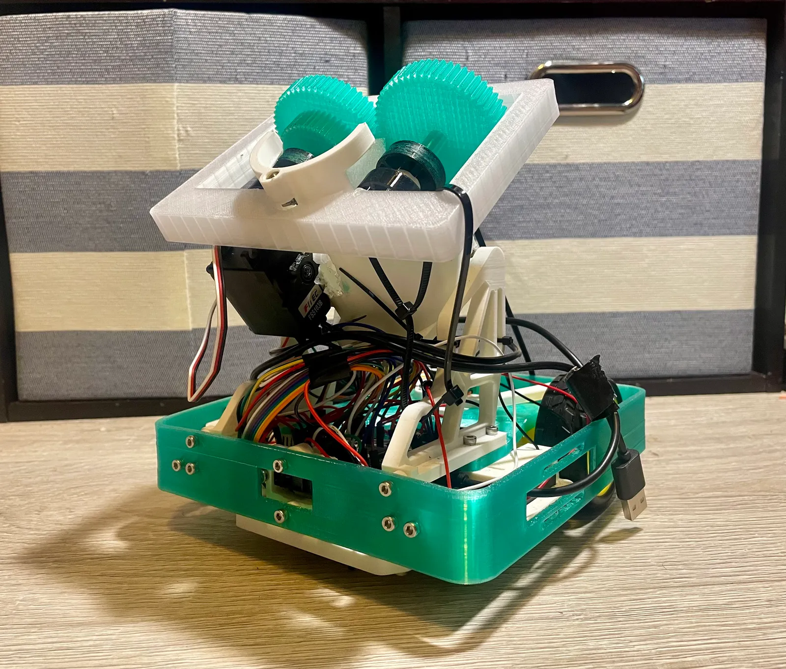 The Robotathon 2025 robot: a 3D-printed teal and white chassis holding a servo, gear train, sensor mounts, and a dense wiring harness.
